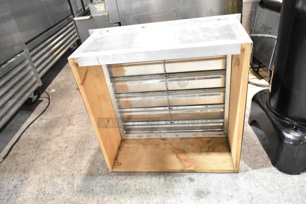 Metal vent with horizontal slats, set in a wooden frame, showcasing a sturdy build. Good condition, industrial setting.