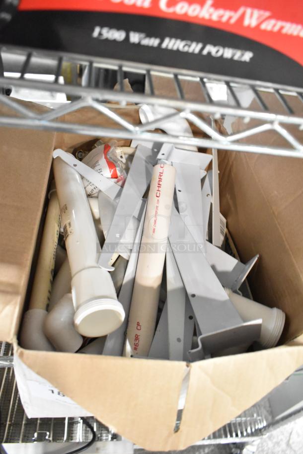 Box of assorted items including metal brackets, extension tubes, a lid, and a hose, all in used condition. Some items labeled "CHARL."
