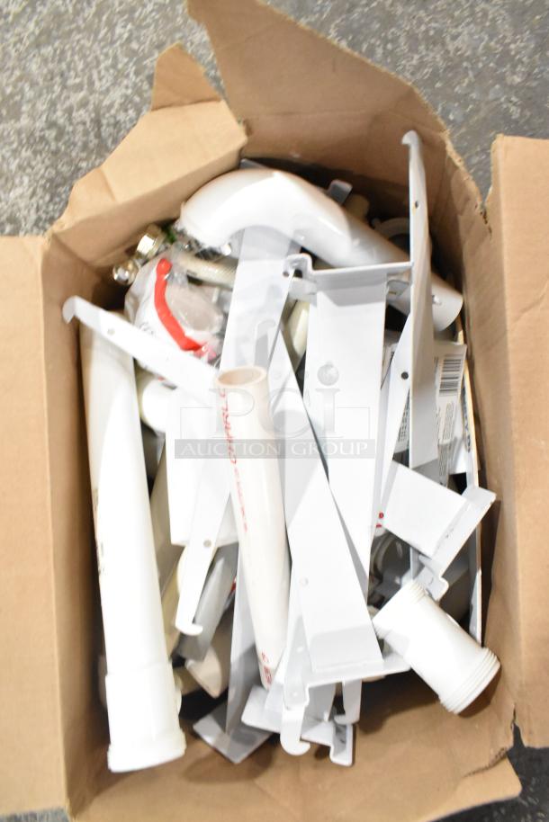 Cardboard box containing assorted items including white brackets, extension tubes, and a hose. Items appear in used condition.