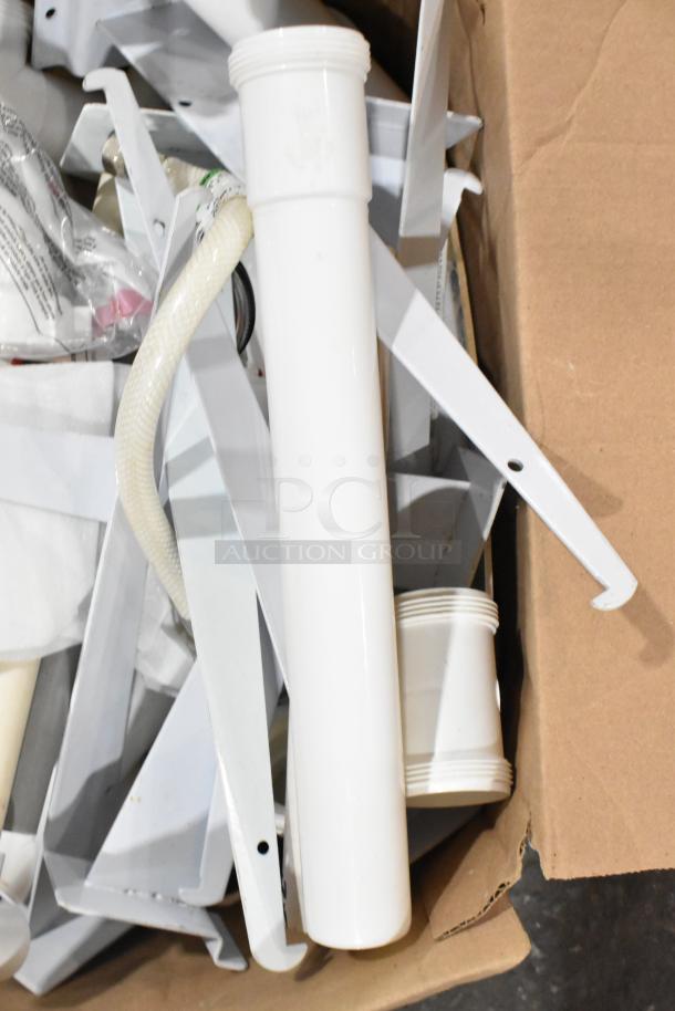 Lot of various items including brackets, a white extension tube, a lid, and a hose in a cardboard box. Mixed condition.