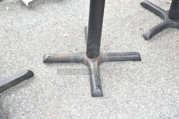 Dining table with a black metal base on concrete. Part of a lot of 13 tables. Sturdy condition, suitable for commercial use.