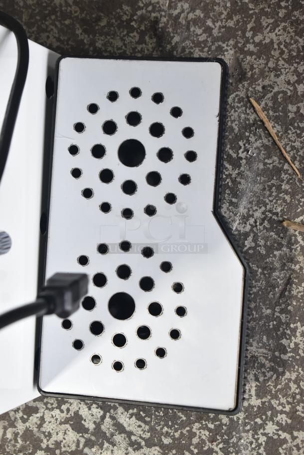 "Commercial steam milk frother base with circular vent holes, brand new with minor scratches and dents, white and black finish."