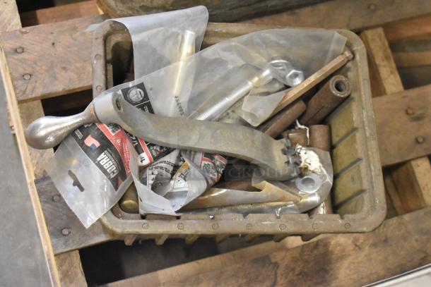 Box of assorted metal machine parts and tools, including levers and screws, on wooden pallet, likely accessories for a milling machine.