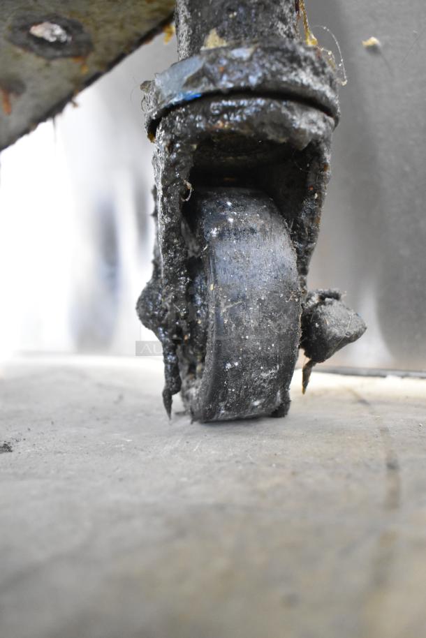 Close-up of a worn caster wheel on a Frymaster FMRE217SC commercial fryer. Visible grease and debris indicate heavy use.