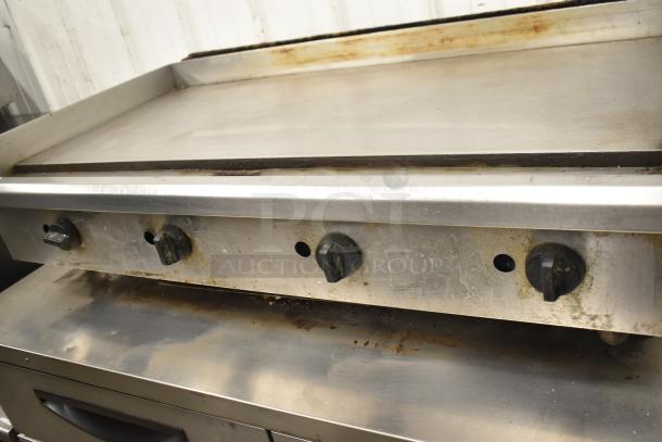 Commercial countertop gas flat top griddle with three control knobs. Slight signs of wear, stainless steel surface.