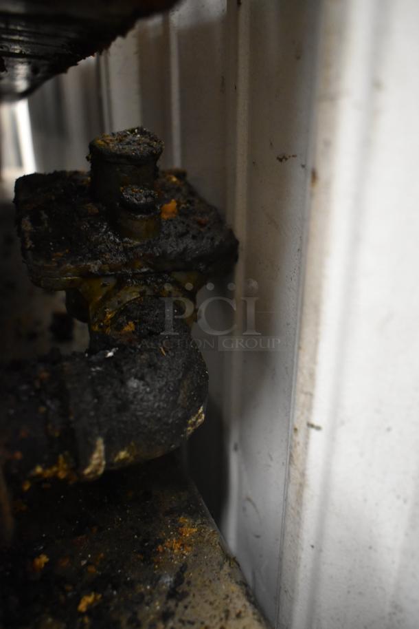 Close-up of a commercial countertop gas griddle's heavily soiled connector and pipe, showing signs of wear and residue buildup.