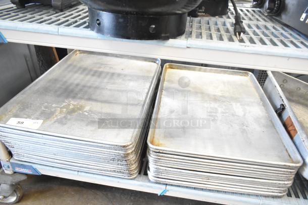 Stack of 31 full-size baking pans and roasting pans, used condition, on metal shelving unit.