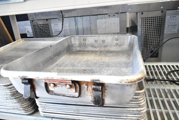 Rustic commercial-grade roasting pan with robust handles, showing signs of wear, stacked on assorted full-size baking pans.