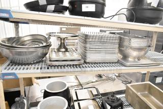 Assorted kitchen items on shelves include metal bowls, baking pans, muffin trays, and colanders. Condition varies.