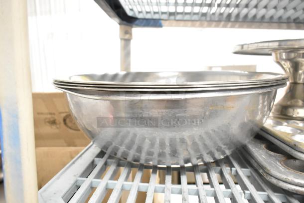 Stainless steel bowls and pans on a wire rack, part of a lot with bowls, baking pans, muffin pans, colanders.