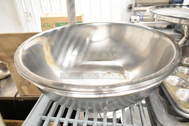 Stainless steel mixing bowl with reflective finish; part of a lot including bowls, pans, and colanders. Moderate wear visible.