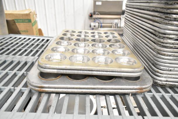 A collection of used baking pans, including muffin trays, stacked on a metal shelf. Part of a 38-item auction lot.