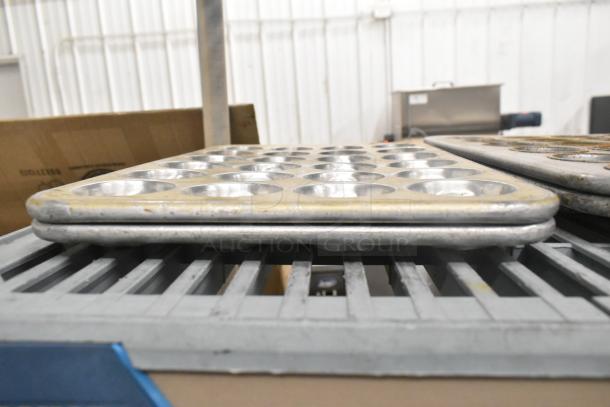 Multiple stacked metal muffin pans in used condition, part of a lot with bowls, baking pans, and colanders auctioned.