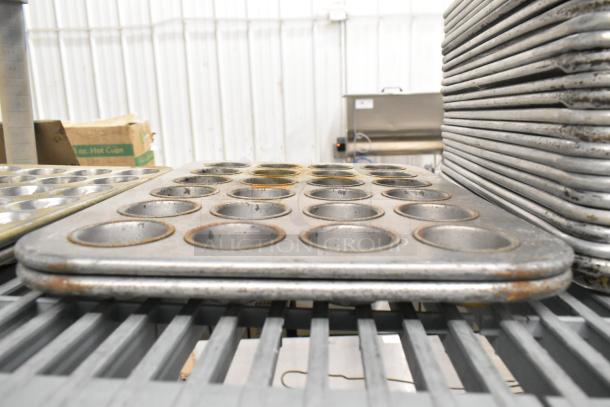 Stacked metal muffin pans, part of a 38-item lot including bowls, baking pans, and colanders for auction.