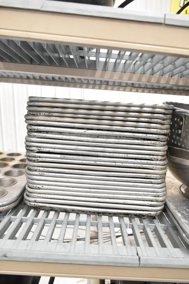 Stack of metal baking pans and muffin trays with a colander, showing signs of use, on industrial shelf.
