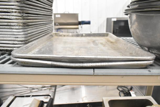 Stack of metal baking sheets and bowls in used condition on a shelf, part of a 38-item kitchenware lot.