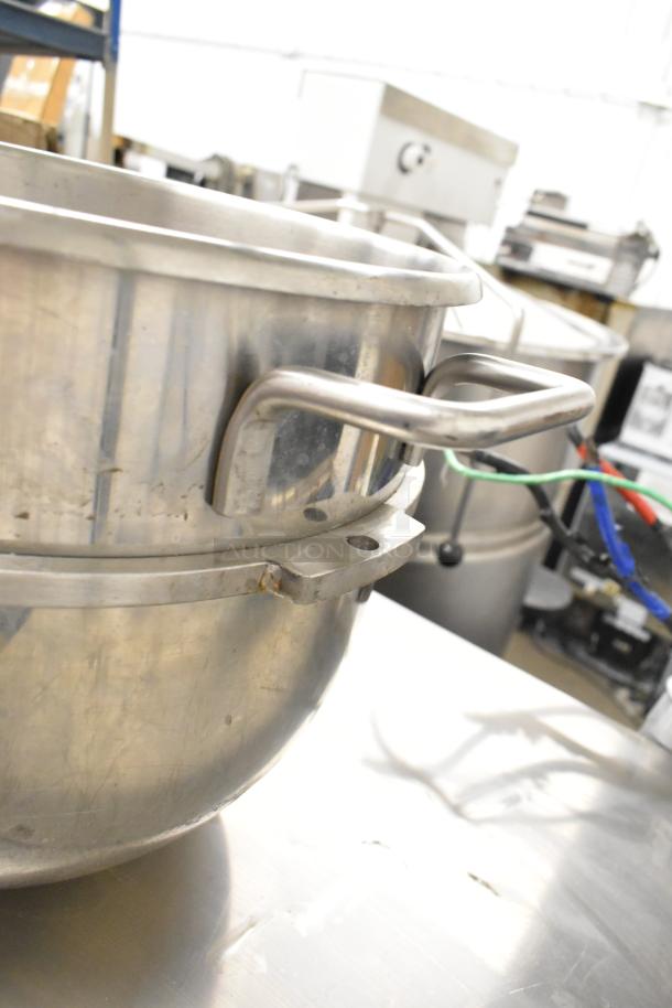 Stainless steel commercial mixing bowl with sturdy handles, showing slight wear. Ideal for heavy-duty kitchen use.