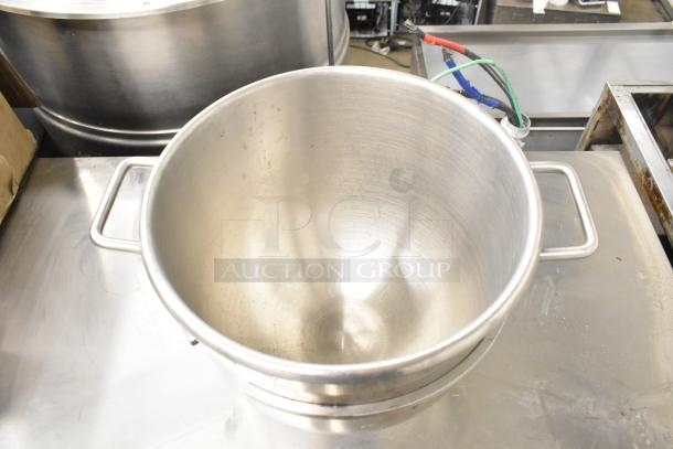 Stainless steel commercial mixing bowl with side handles, showing light wear, placed on a stainless steel surface.
