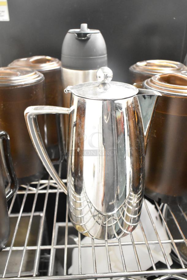 Auction lot of kitchen items including a stainless steel pitcher, brown containers, and a thermal carafe on a metal shelf.