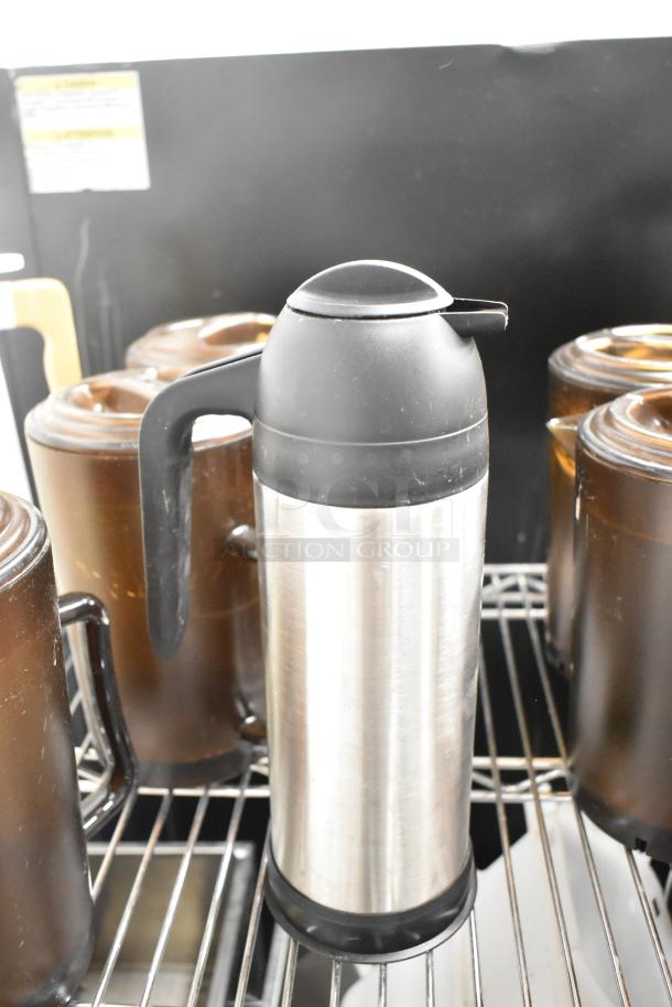 Stainless steel pitcher with black plastic handle and lid, surrounded by brown containers on wire shelving. Shelving not included.