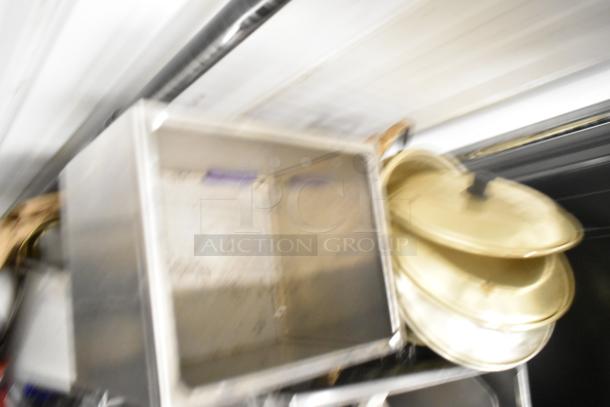 Blurred image of an auction lot with metal drop-in bins, stack of poly pitchers, cutting boards, and rice cooker inserts. No shelving included.