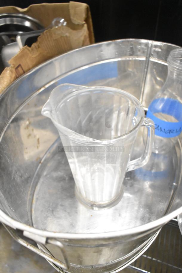 Metro lot with poly pitchers, metal bins, and rice cooker inserts, in used condition. Blue labeled transparent bottle visible.