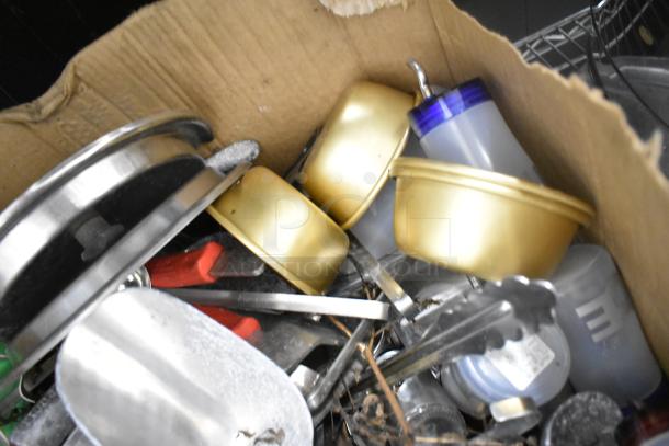 Assorted kitchen items in a cardboard box, includes drop-in bins, poly pitchers, cutting boards, rice cooker inserts, utensils.