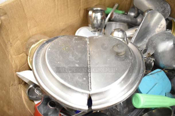 Assorted kitchen items in a box, including silver lids, utensils, and colorful handles. Condition shows wear. No shelving unit.