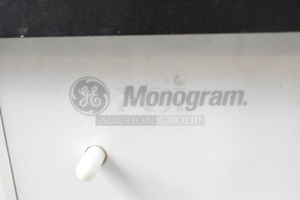 General Electric Monogram logo on GE ZDIS150WSS E built-in ice maker, white panel, slight wear visible.