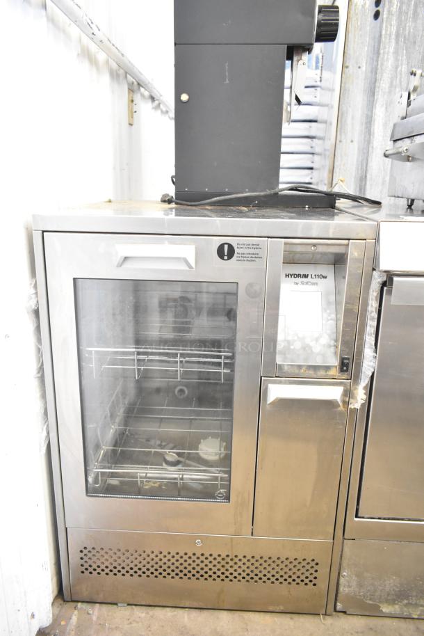 SciCan Hydrim L110W commercial washer with glass door, shows interior racks. Metal exterior with visible display panel.