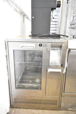 SciCan Hydrim L110W commercial washer with glass door, shows interior racks. Metal exterior with visible display panel.