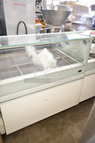 Commercial floor-style gelato display case merchandiser with glass top, multiple trays, and sturdy build, showing slight wear.