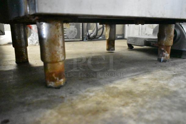 Bottom view of a commercial smoking cabinet with rusted metal legs on a concrete floor, indicating use and age.