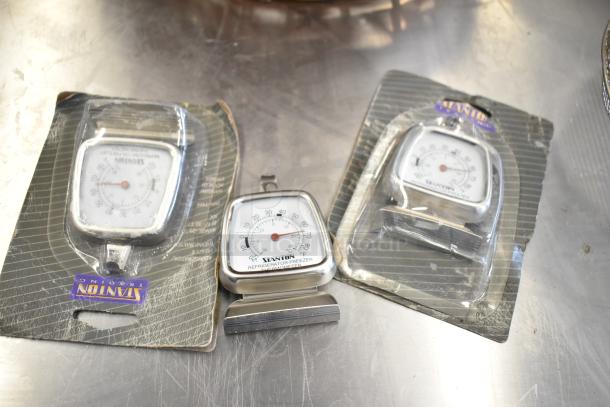 Three Stanton refrigerator-freezer thermometers in packaging on a metal surface. Include temperature gauge detail.