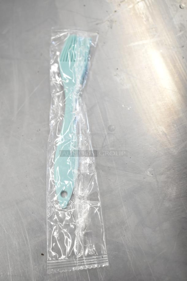 Sealed aqua plastic fork and knife set in transparent packaging on a metal surface.