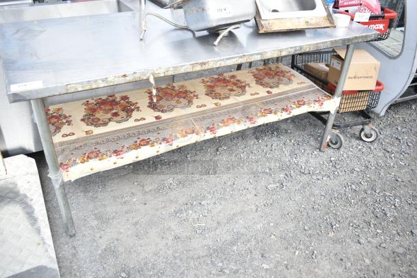 Commercial metal table with under shelf, visible rust and wear, floral-patterned liner on shelf, overall used condition.