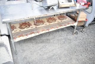 Commercial metal table with under shelf, visible rust and wear, floral-patterned liner on shelf, overall used condition.
