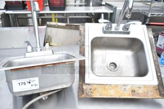 Two single bay drop-in sinks, stainless steel, with faucets, visible surface rust and wear, auction item label attached.