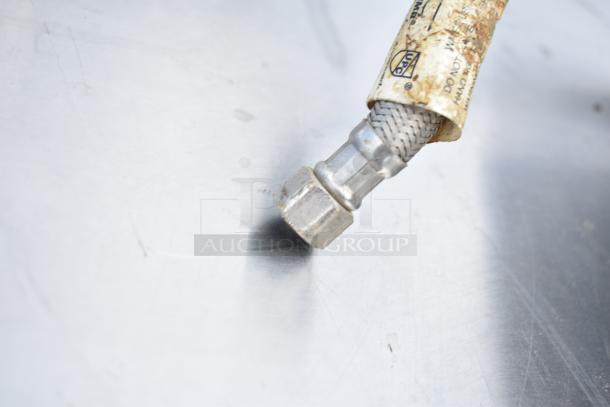 Close-up of a stainless steel braided connector on 2 single bay drop-in sinks; visible label with UPC certification.