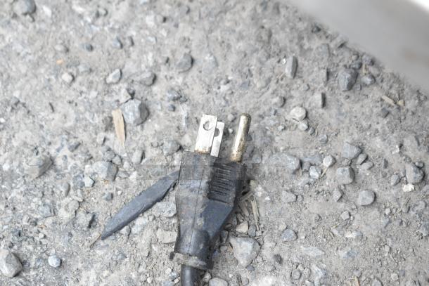 A power plug on a gravel surface, suggesting wear, possibly from one of the mini coolers for auction.