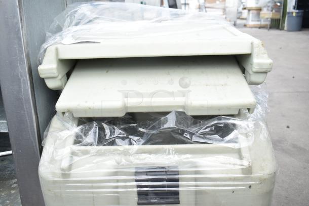 Cambro tan poly portable ice bin with lid, on commercial casters. Slight wear visible. Wrapped in plastic for protection.