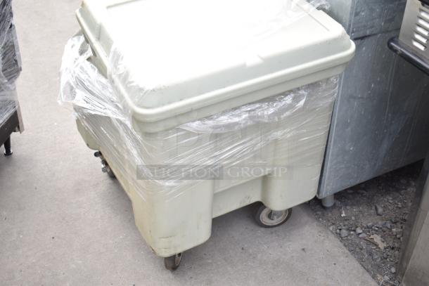 Cambro tan poly portable ice bin on commercial casters, wrapped in plastic, showing signs of outdoor wear.