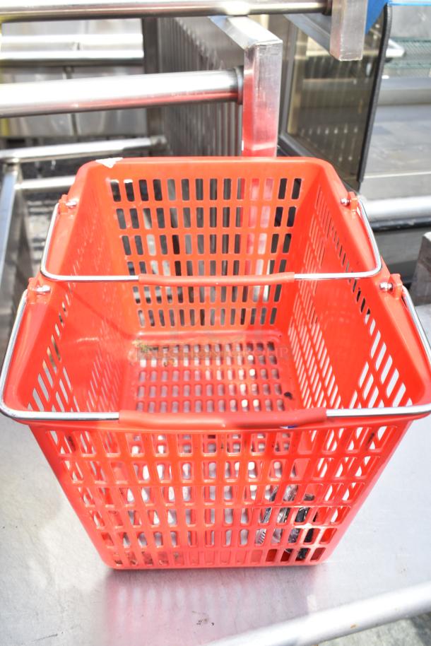 Red plastic shopping basket with metal handles. Grid design for ventilation. Light wear, suitable for retail or storage use.