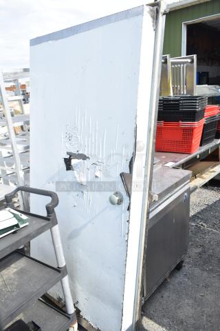 Damaged walk-in door with peeling paint and impact marks, metal frame, and a rounded knob. Visible wear indicates heavy use.