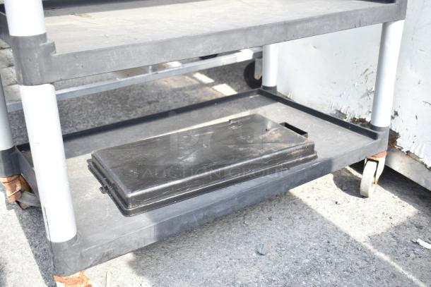 Black poly 3-tier cart with commercial casters, showing wear on surfaces. Ideal for storage and transport. Appears durable.