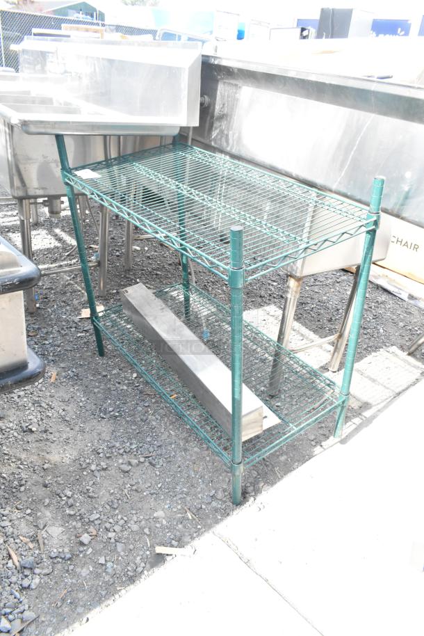 Green finish 2-tier wire shelving unit, sturdy metal construction, outdoor setting. Buyer must dismantle; consider freight costs.