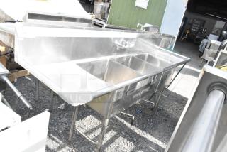 Stainless steel commercial 3 bay sink with dual drain boards, labeled "Wash." Used, in good condition.