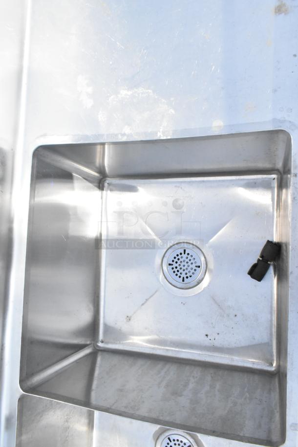 Commercial 3-bay stainless steel sink with dual drain boards, showing slight wear. Ideal for restaurant use.