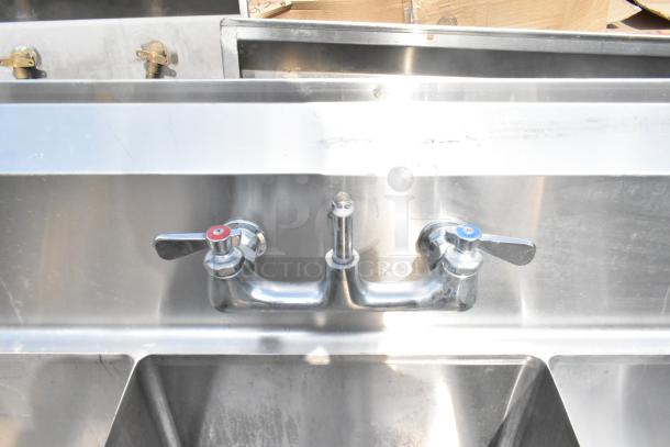Commercial stainless steel 3 bay sink with dual drain boards, red and blue faucet knobs, visible wear on the surface.
