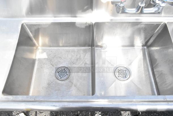 Commercial 3 bay stainless steel sink with dual drain boards, slight surface wear, dual faucets visible.